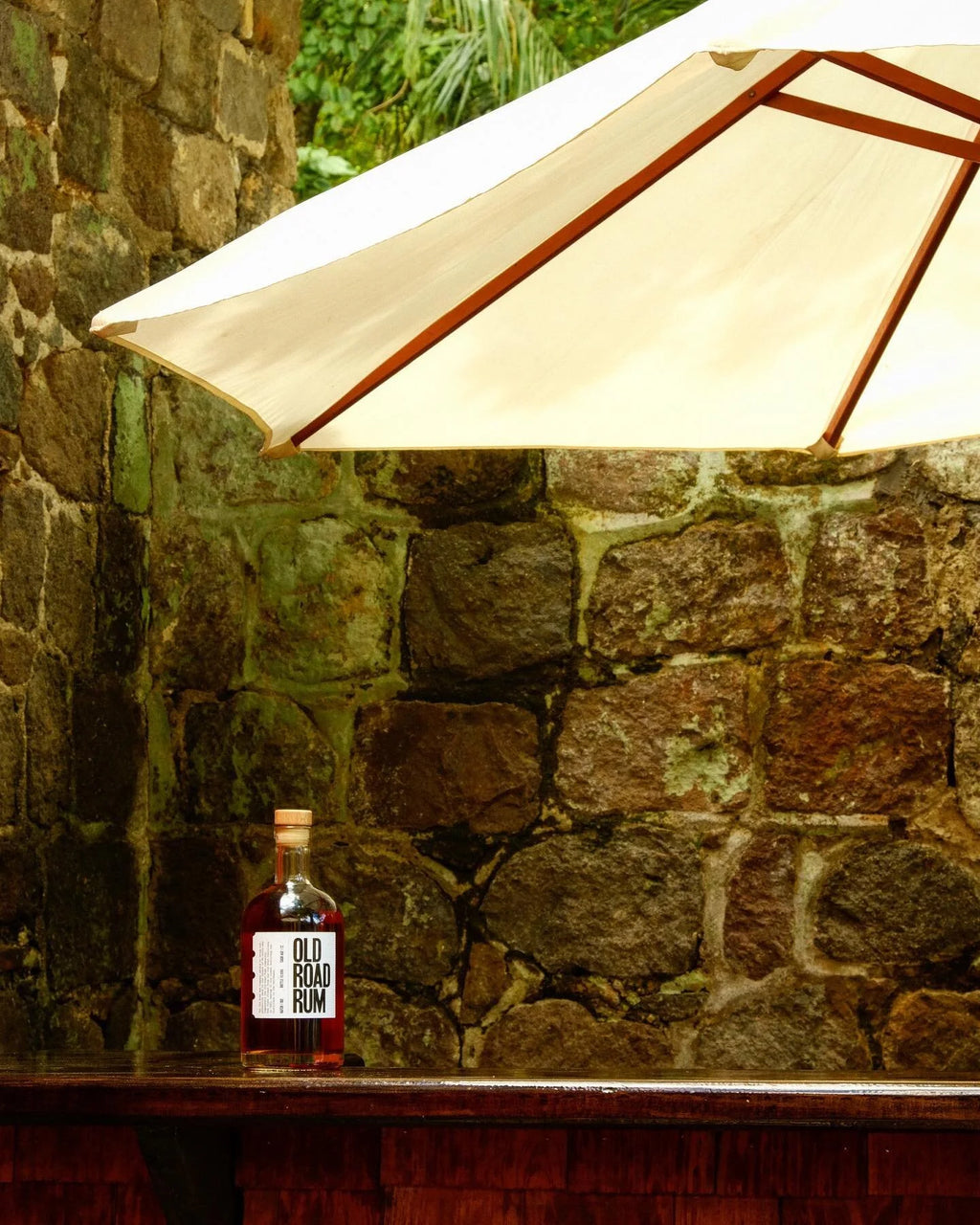 Old Road Rum 12-year on the bar at Wingfield Estate, canvas umbrella against the seventeenth-century stone wall